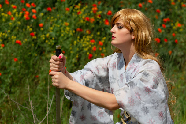 Young asian woman in traditional kimono trains fighting techniques with katana sword on the hills with red poppies, samurai warrior girl - Foto, Bild