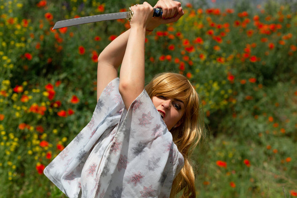 Young asian woman in traditional kimono trains fighting techniques with katana sword on the hills with red poppies, samurai warrior girl - Valokuva, kuva