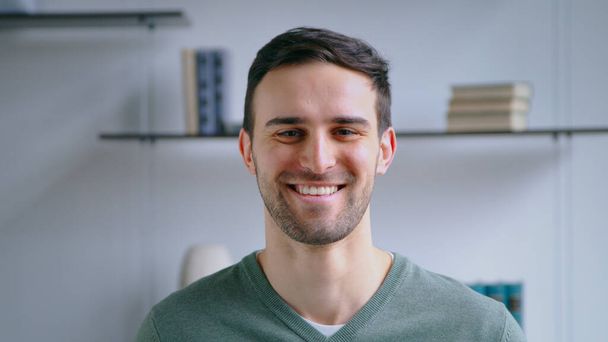 Молодой улыбающийся мужчина смотрит в камеру в офисе - Фото, изображение