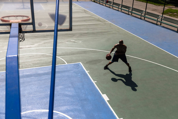 One african-american male basketball player training at street public stadium, sport court or palyground outdoors. Concept of healthy active lifestyle, motion, hobby. - Foto, imagen