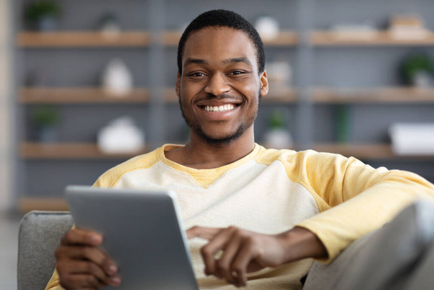 alegre negro chico descansando con digital tablet en sofá - Foto, Imagen
