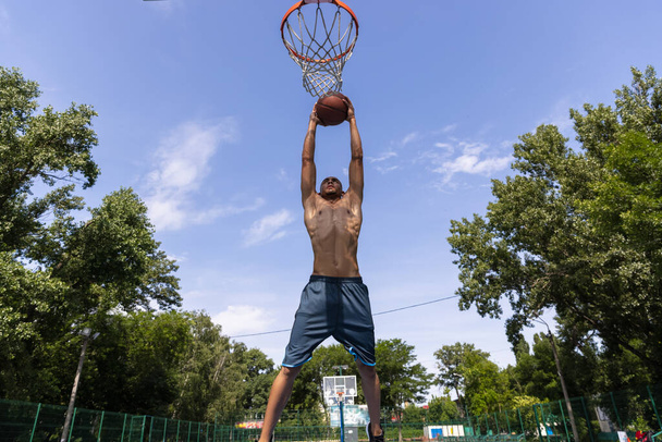 Young man, muscular african male basketball player playing basketball at street public stadium, sport court or palyground outdoors. Summer sport games. - Fotó, kép