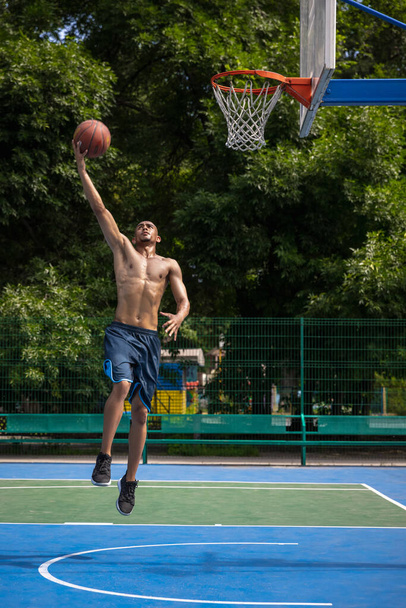 Young man, muscular african male basketball player playing basketball at street public stadium, sport court or palyground outdoors. Summer sport games. - Zdjęcie, obraz