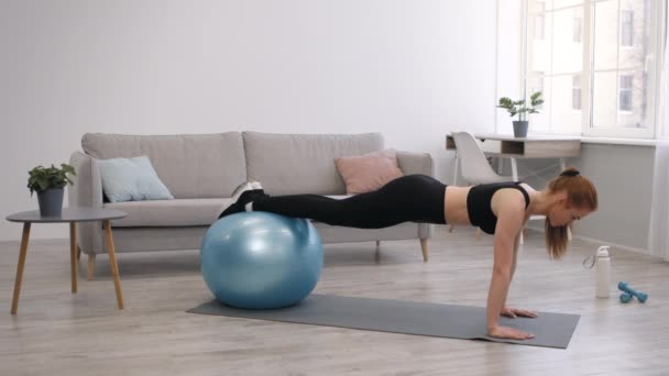 Atlética dama de pie en el tablón de ejercicio con Fitball en casa - Imágenes, Vídeo