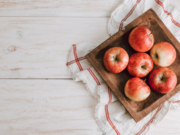 Äpfel in einer Obstschale mit Küchenserviette liegen rechts auf einem Holztisch mit Platz für Text links, Großaufnahme von oben. - Foto, Bild