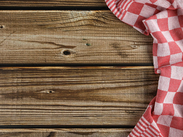 Una servilleta de cocina roja a cuadros se encuentra a la derecha en una mesa de madera marrón con espacio para el texto a la izquierda, una vista superior de cerca. - Foto, Imagen