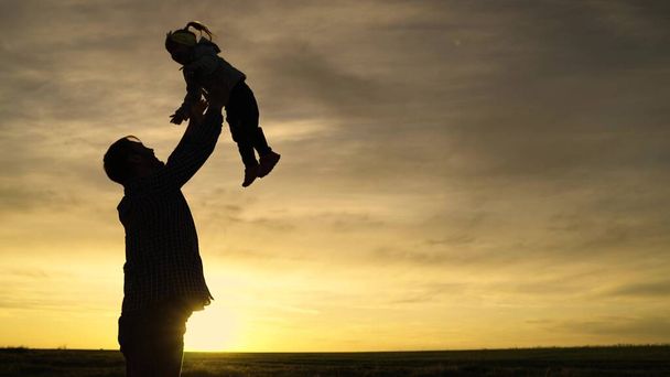 Silhouette Dad tosses his happy daughter into blue sky. Happy family holiday. Father and little child play, laugh, hug together. Enjoyable family travel. Baby is in arms of the parents. Dads day off - Photo, Image