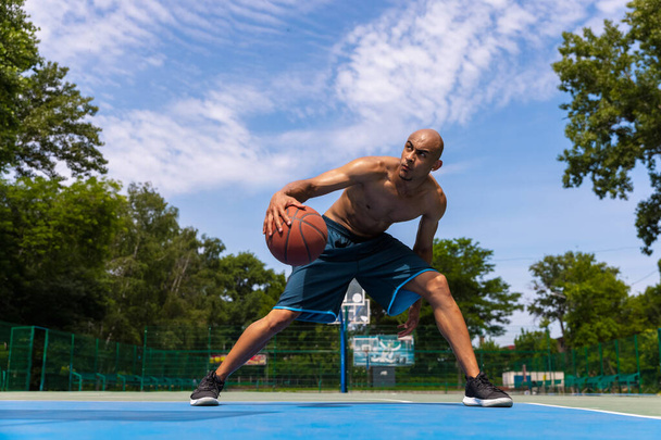 Strong muscular african-american male basketball player training at street public stadium, sport court or palyground outdoors. Summer sport games. - Photo, image