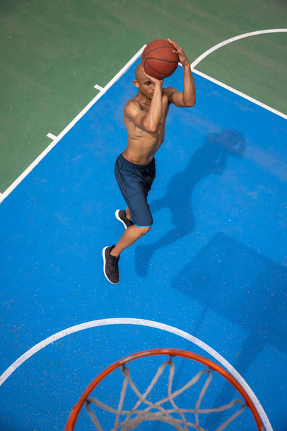 Top view of young man, male basketball player playing basketball at street public stadium, sport court or palyground outdoors. Summer sport games. - Valokuva, kuva