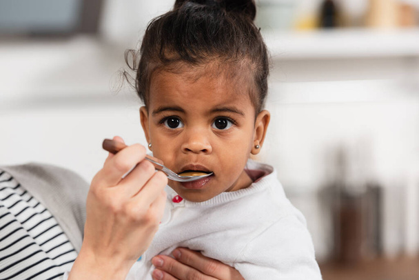 madre sosteniendo cuchara y alimentación adoptiva afroamericana hija - Foto, imagen
