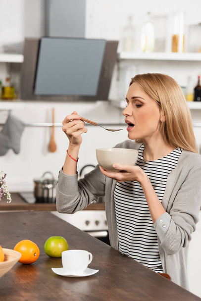 blonde woman eating breakfast in kitchen - Foto, afbeelding
