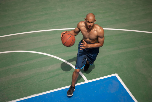 Strong muscular african-american male basketball player training at street public stadium, sport court or palyground outdoors. Concept of healthy active lifestyle, motion, hobby. - Fotó, kép