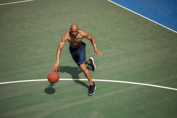 Top view of young man, male basketball player playing basketball at street public stadium, sport court or palyground outdoors. Summer sport games. - Foto, Bild