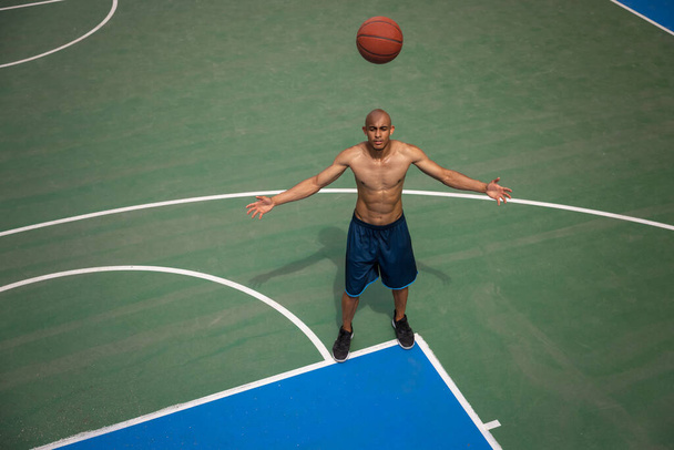 Κάτοψη του νεαρού, του ανδρικού μπασκετμπολίστα που παίζει μπάσκετ στο δημόσιο γήπεδο του δρόμου, στο γήπεδο του αθλητισμού ή σε προαύλιο χώρο. Καλοκαιρινά αθλητικά παιχνίδια. - Φωτογραφία, εικόνα