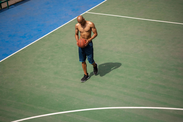One african-american male basketball player playing at street public stadium, sport court or palyground outdoors. Concept of healthy active lifestyle, motion, hobby. - 写真・画像