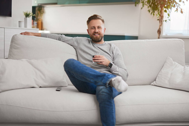 Happy man with drink resting on sofa - Fotoğraf, Görsel