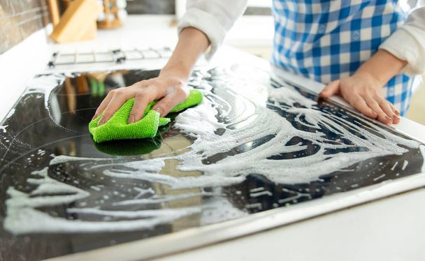 Unrecognizable woman cleaning glass induction stove with a detergent and a cleaning sponge - Foto, Imagen