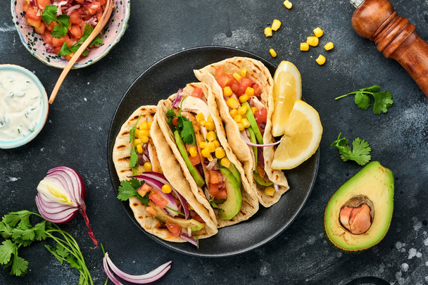 Mexican tacos with grilled chicken, avocado, corn kernels, tomato, onion, cilantro and salsa at black stone table. Traditional Mexican and Latin american street food. Top view. - Foto, Bild