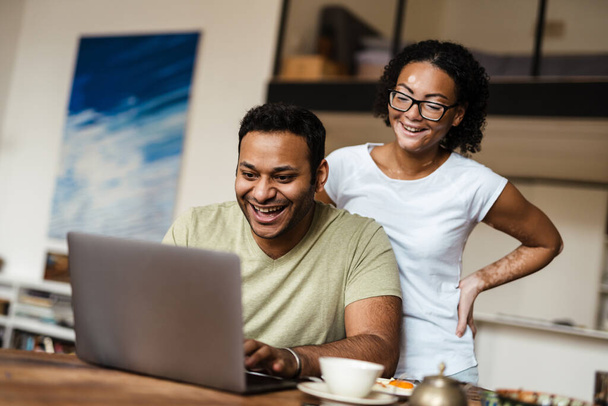 Близькосхідний чоловік і жінка посміхаються під час роботи з ноутбуком вдома
 - Фото, зображення