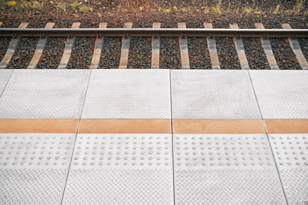 Trein platform bestrating vloer met patroon. Station met gele geleiding hobbels en lijnen voor de slechtzienden. Stalen rails. - Foto, afbeelding