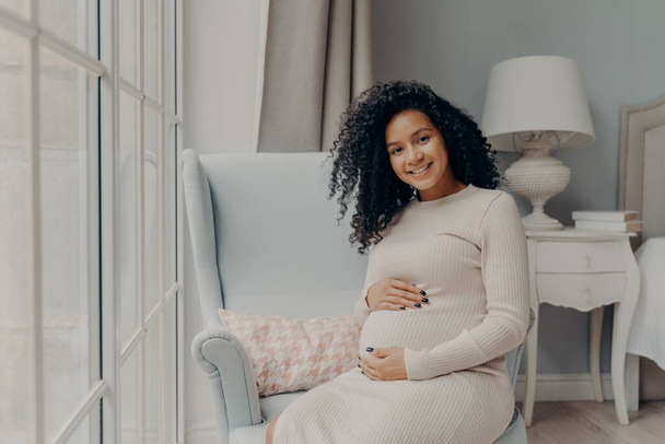 Positive pregnant woman touching gently her belly and smiling - Photo, Image