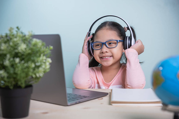 Concept learning online social distance. Asian kids girls wearing glasses, headphones smile happily looking at a laptop. Listen to online lessons from teachers. learning from home in the room personal - Photo, Image