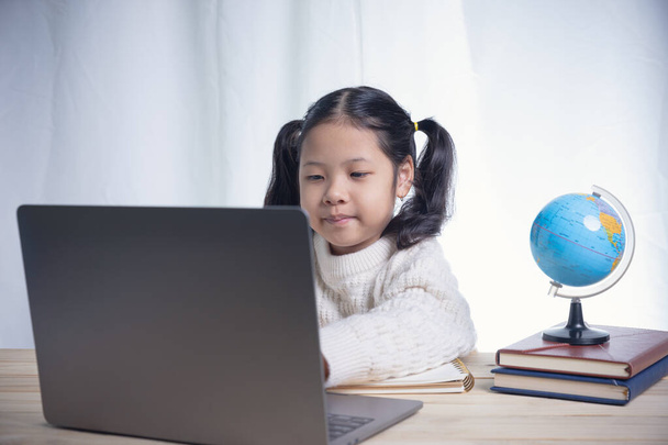 Asijské dítě dívka psaní následuje učitel pro učení on-line lekce podle videa volejte na internet z notebooků v místnosti. Šíření koronaviru donutilo studenty studovat online z domova. - Fotografie, Obrázek