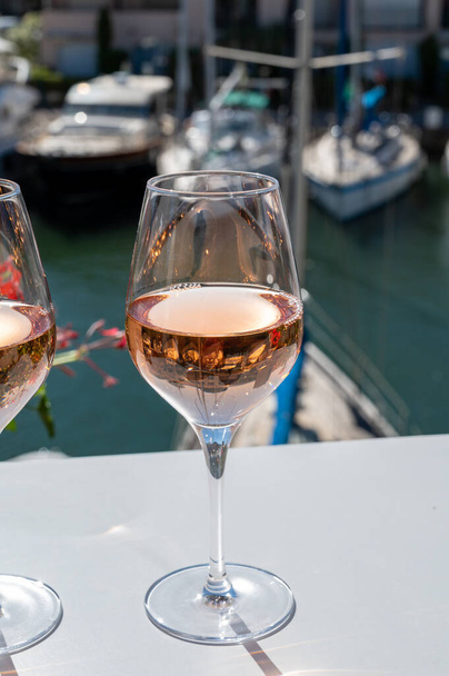 コート・ド・プロヴァンスの冷たいバラワインを飲みながら、夏はコート・ド・プロヴァンスの冷たいバラのワインを、船やヨットを背景にフランスのヴァール州ポート・グリモーの日当たりの良い屋外テラスでお楽しみください。 - 写真・画像