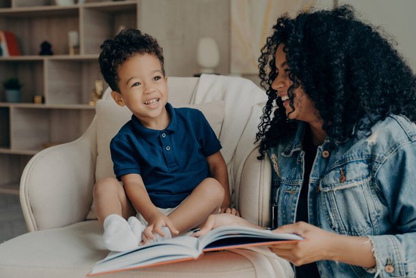 Lovely afro american mother reading book to her little son and laughing - Photo, Image