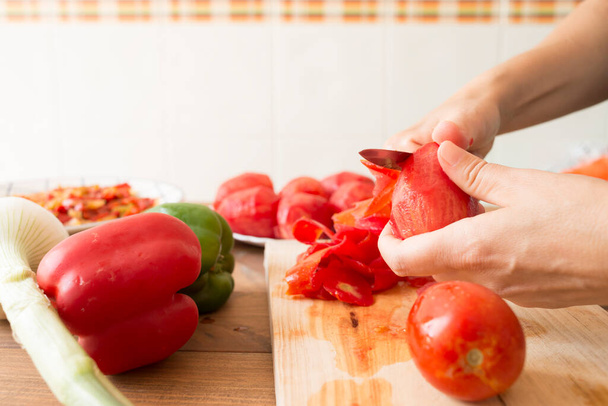 Detail of a woman's hands peeling tomatoes with a knife. Preparation of roasted peppers, a typical dish of Spanish and Andalusian cuisine. - Фото, изображение