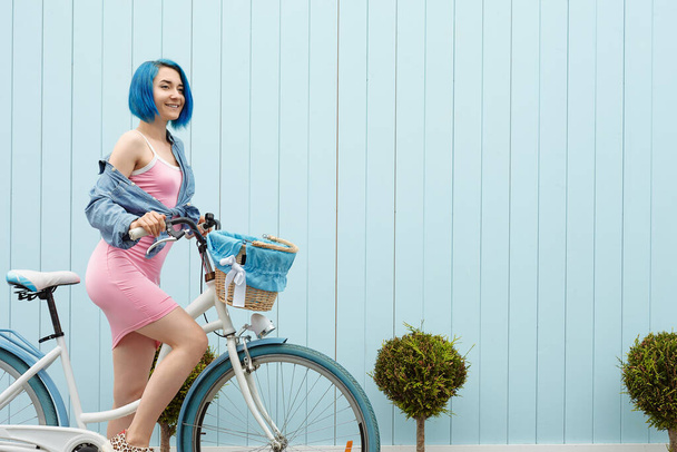 Jolie fille sur un vélo blanc avec un busket sur le mur bleu. Côté sud près de la mer en saison estivale. - Photo, image