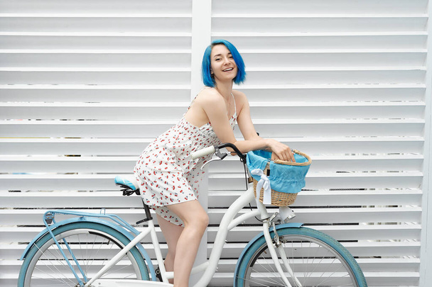 Jolie fille sur un vélo blanc avec un busket sur le mur blanc. Côté sud près de la mer en saison estivale. - Photo, image
