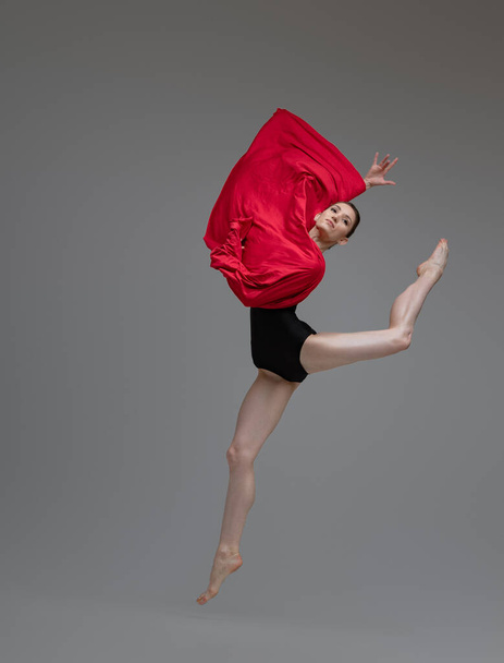 Jumping ballerina in tutu holding red silk - Фото, зображення
