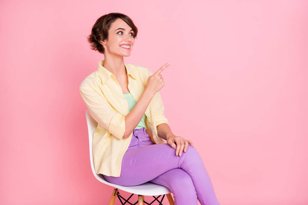 興奮したかなり若い女性の写真黄色のシャツ座って椅子を着用空のスペース孤立ピンク色の背景を指す - 写真・画像