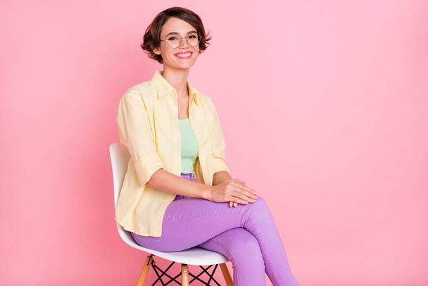 Photo of cute adorable young lady dressed yellow shirt spectacles sitting chair isolated pink color background - Foto, immagini