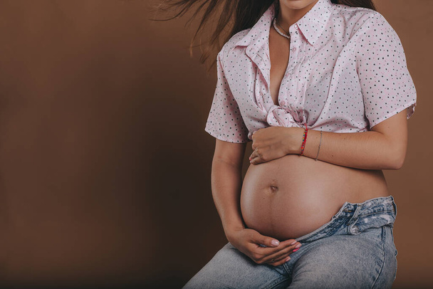 pregnant woman in jeans and a shirt holds her belly with her hands. - Foto, Imagen