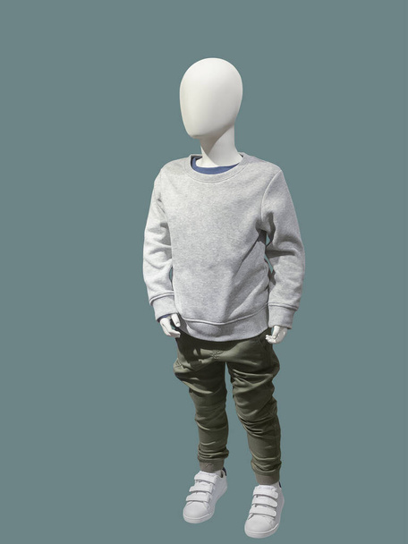 Imagem de comprimento total de um manequim de exibição infantil vestido com camisola cinza e calças cáqui isoladas em um fundo azul. - Foto, Imagem