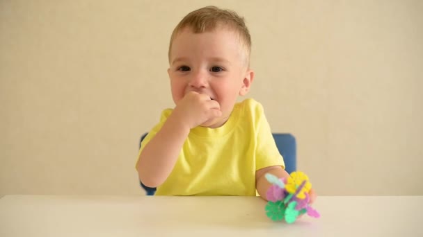 maluch bawi się w konstruktora siedząc przy białym stole. gra edukacyjna Montessori grzywny umiejętności motoryczne. wczesna koncepcja rozwoju. bierze niebezpieczne zabawki do ust. - Materiał filmowy, wideo