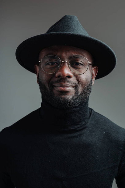 Portrait of handsome african american man in black turtleneck with hat and glasses smiling - Фото, изображение