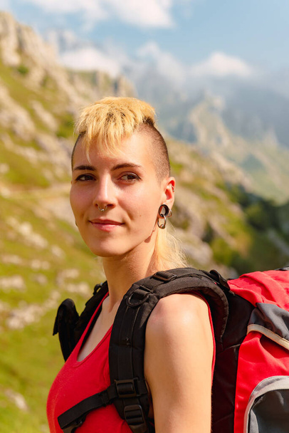 若い白人女性が笑顔で山を背景にスポーツをしている姿が描かれています。バックパックを持ったハイカーの人. - 写真・画像
