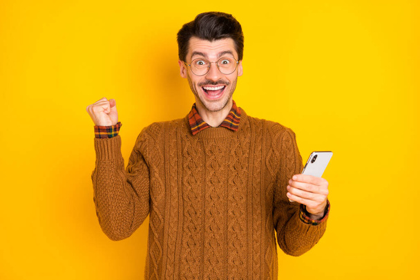 Photo of amazed excited young man raise hand fist win smartphone notifications isolated on yellow color background - Фото, зображення