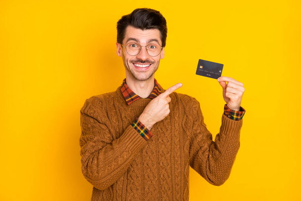 Portrait of positive guy indicate finger debit card toothy smile wear pullover isolated on yellow color background - Foto, immagini