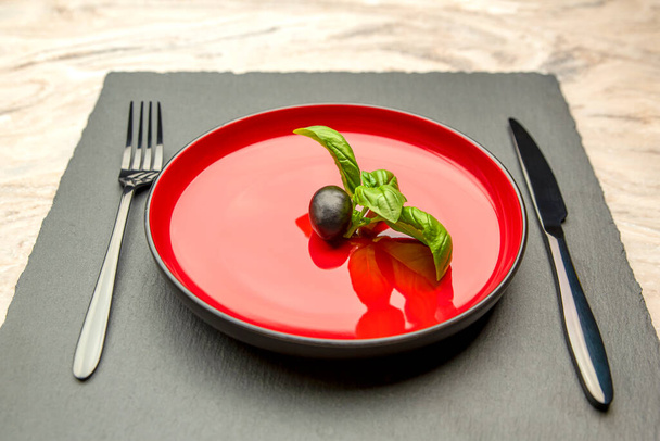 Dieta. Pequeña cantidad de comida en el plato. Una aceituna está en un plato rojo, un cuchillo y un tenedor. La pérdida de peso y el concepto de dieta. Espacio vacío para texto - Foto, imagen