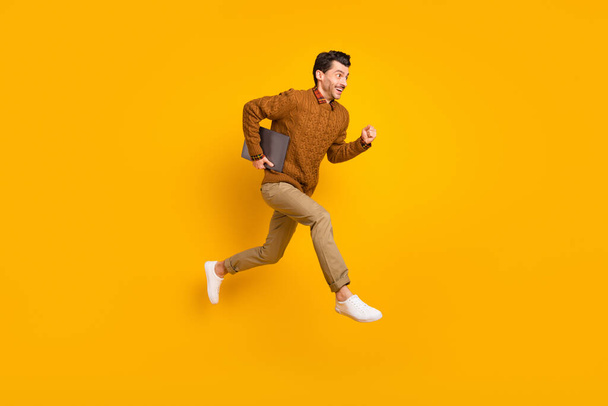 Full size profile photo of impressed nice brunet man hold laptop run wear sweater isolated on yellow background - Foto, Imagen
