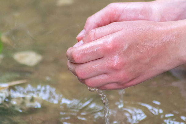 Мальчик играет с чистой водой в маленьком ручье, используя руки и источник воды, охлаждающий его руки и освежающий чистым эликсиром жизни для медитации дзен или охраны окружающей среды - Фото, изображение