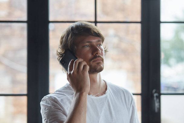 El hombre barbudo habla por teléfono con amigos o colegas, se relaja, disfruta de la comunicación remota. - Foto, Imagen