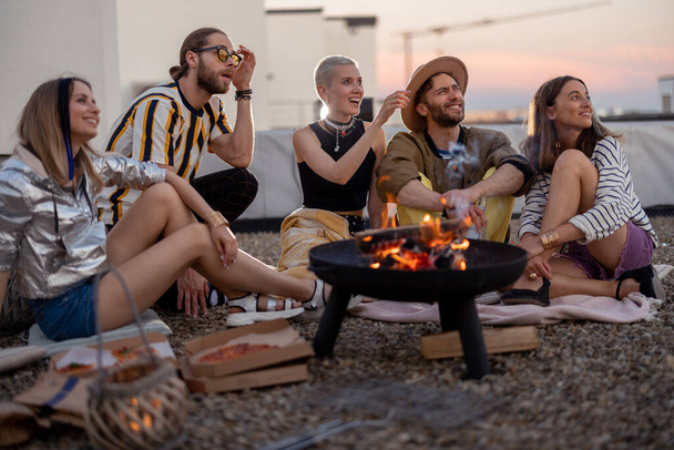 Friends by a fireplace on the rooftop at sunset - Фото, изображение