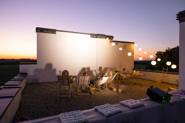 Люди смотрят кино на террасе на крыше на закате - Фото, изображение