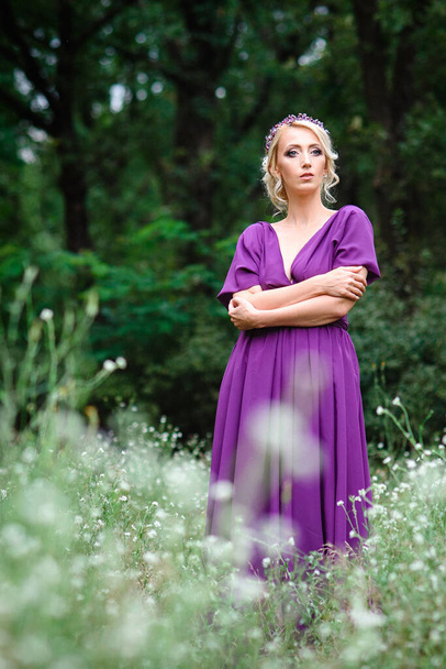 Girl model blonde in a lilac dress with a bouquet with a green forest - Photo, Image