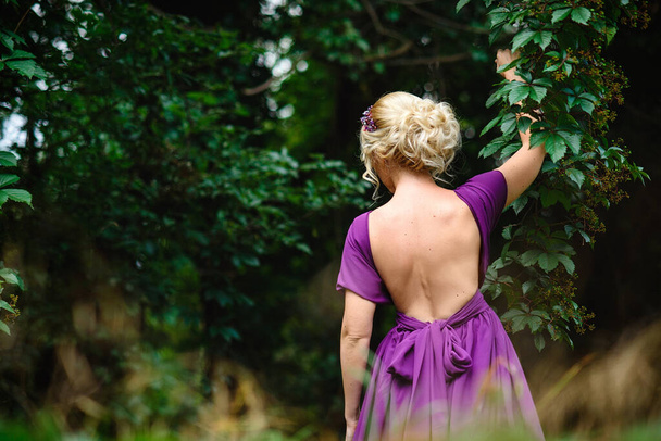 Girl model blonde in a lilac dress with a bouquet with a green forest - Foto, Imagem